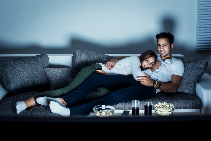 Young couple watching a movie at home, lying on sofa. Both Caucasian, casual, about 25 years old.