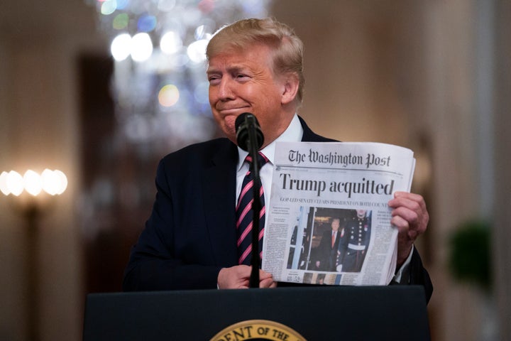 President Donald Trump holds up a newspaper trumpeting his acquittal as he spoke in the East Room of the White House on Thurs