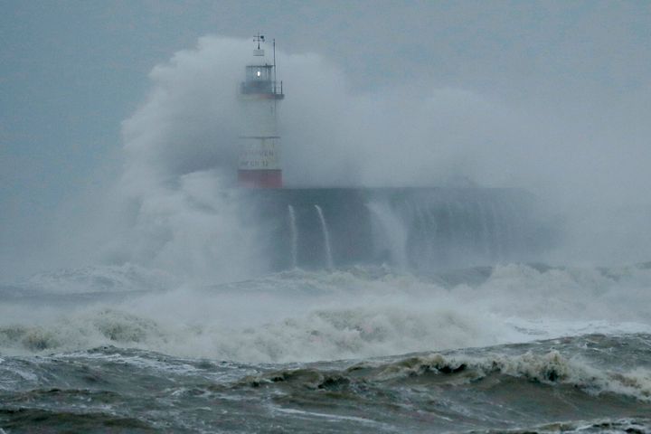 Waves crash over the harbour and a lighthouse in Newhaven on the south coast of England.