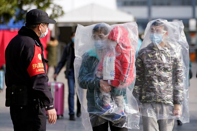 Passengers wearing masks and covered with plastic bags walk outside the Shanghai railway station in Shanghai,...