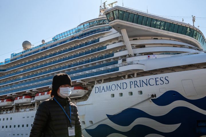 A member of the media wearing a face mask walks past the Diamond Princess cruise ship at Daikoku Pier where it is being resupplied and newly diagnosed coronavirus cases taken for treatment as it remains in quarantine after a number of the 3,700 people on board were diagnosed with coronavirus, on February 10, 2020 in Yokohama, Japan.