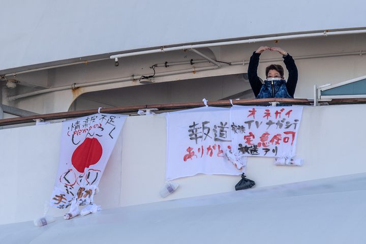 A passenger gestures after hanging a banner reading "please broadcast this on TV" (R) next to banners reading "thank you for reporting this" (C) and "shortage of medicine" (L) on the Diamond Princess cruise ship at Daikoku Pier where it is being resupplied and newly diagnosed coronavirus cases taken for treatment as it remains in quarantine, February 10, 2020 in Yokohama, Japan. 