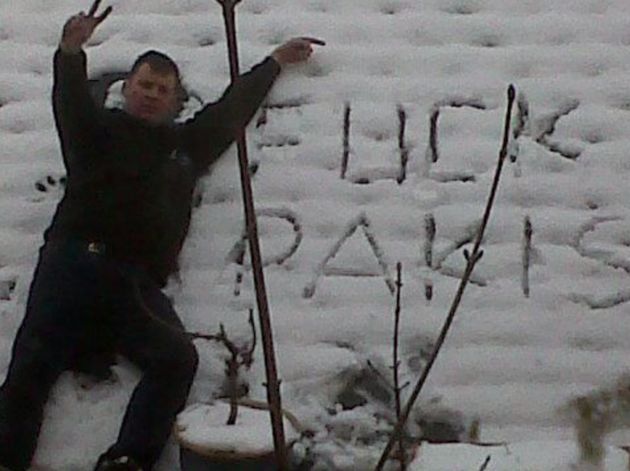 Andrew Foster posing next to a racist sign which says 'f*** pakis' 