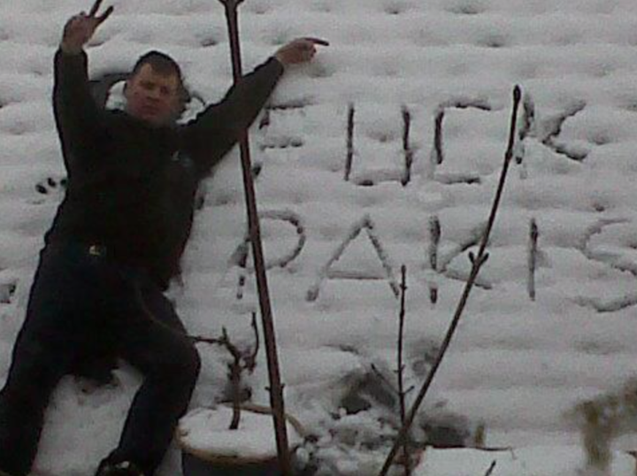 Andrew Foster posing next to a racist sign which says 'f*** pakis' 