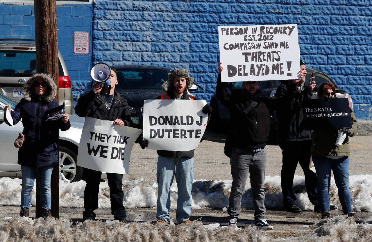 Demonstrators, including one with a sign comparing Trump to Philippine President Rodrigo Duterte, protest across the street as the U.S. president visits a firehouse in Manchester, New Hampshire, during a trip devoted to the issue of combating the opioid crisis on March 19, 2018.