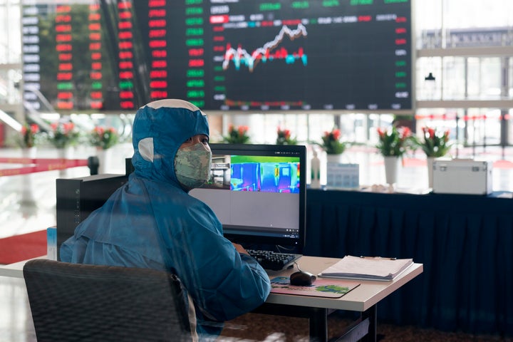 Un trabajador del mercado de cambio de Shanghai, con un traje de protección y controlando la temperatura de las demás personas.