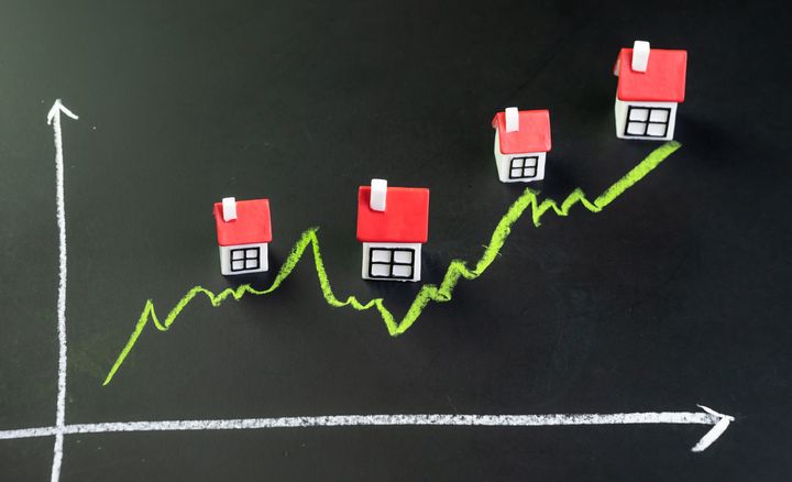 House, property or real estate market price go up or rising concept, small miniature house with green line graph going up on black chalkboard.
