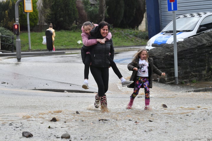 Local residents remain cheerful as walk through receding floodwater in Mountain Ash, Wales as Storm Dennis hit the UK.