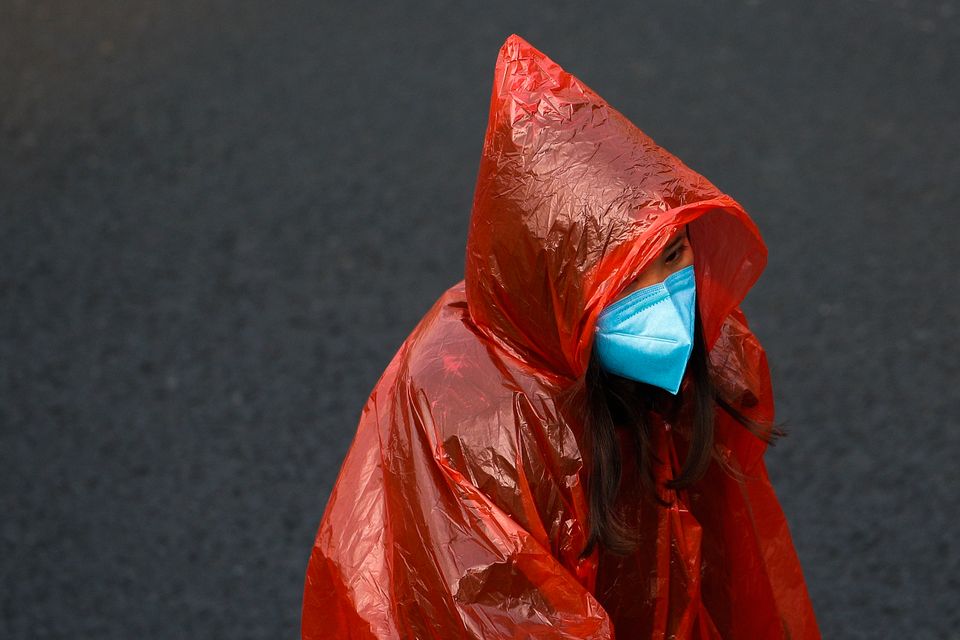 A masked woman in a plastic rain coat walks on a street in Beijing, Tuesday, Feb. 11.