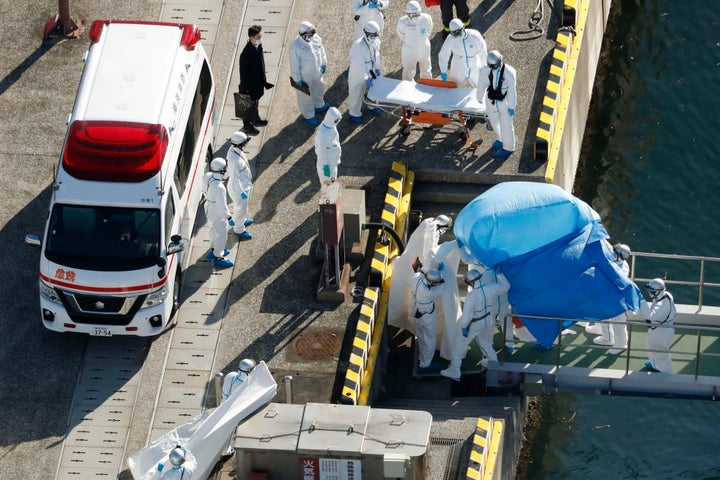 Medical workers in protective suits lead a passenger who tested positive for a new coronavirus on the Diamond Princess cruise ship on Wednesday, Feb. 5.