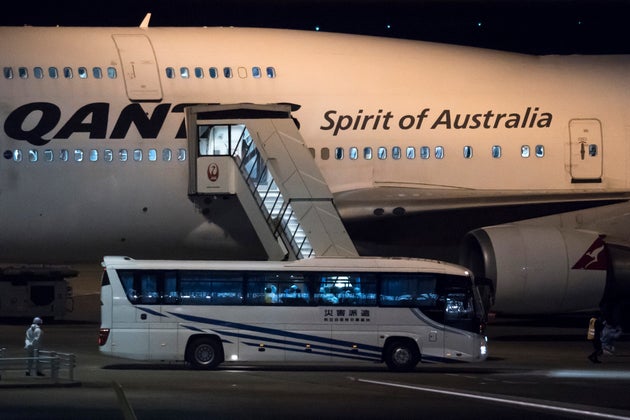 A worker wearing a protective suit stands next to a bus carrying passengers, who boarded the Qantas aircraft chartered by the Australian government, from the quarantined Diamond Princess cruise ship drive at Haneda airport on February 19, 2020 in Tokyo, Japan.