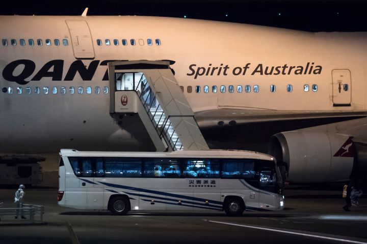 A worker wearing a protective suit stands next to a bus carrying passengers, who boarded the Qantas aircraft chartered by the Australian government, from the quarantined Diamond Princess cruise ship drive at Haneda airport on February 19, 2020 in Tokyo, Japan. 