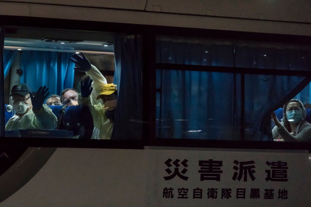 People wave from a bus carrying passengers, who boarded the Qantas aircraft chartered by the Australian government, from the quarantined Diamond Princess cruise ship drive at the Daikoku Pier on February 19, 2020 in Yokohama, Japan.