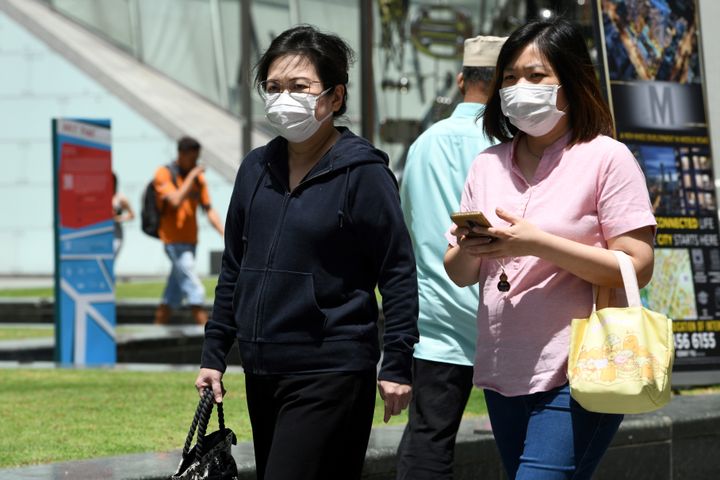 Two women wearing protective facemasks, amid concerns over the spread of the COVID-19 coronavirus, walk on the street in Singapore on February 14, 2020. 