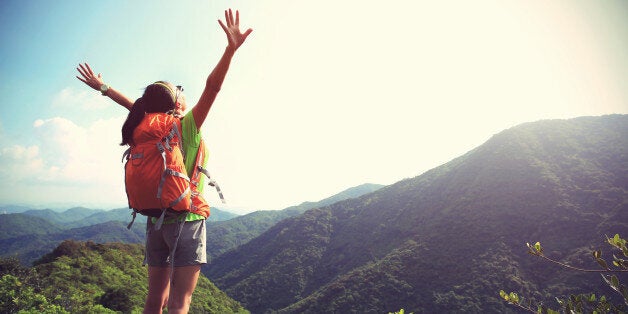 cheering woman hiker open arms at mountain peak cliff