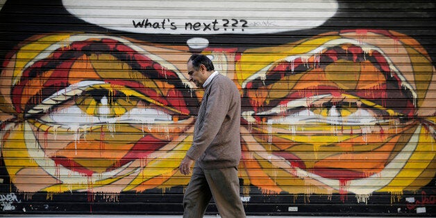 In this photo made on Tuesday, April 29, 2015, a Greek man walks past a graffiti in central Athens. Wednesday May 6 marks fiv