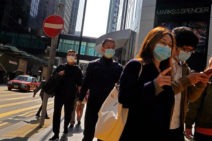 People wearing face mask walk at a downtown street in Hong Kong Friday, Feb. 21, 2020. COVID-19 viral illness has sickened tens of thousands of people in China since December. (AP Photo/Vincent Yu)