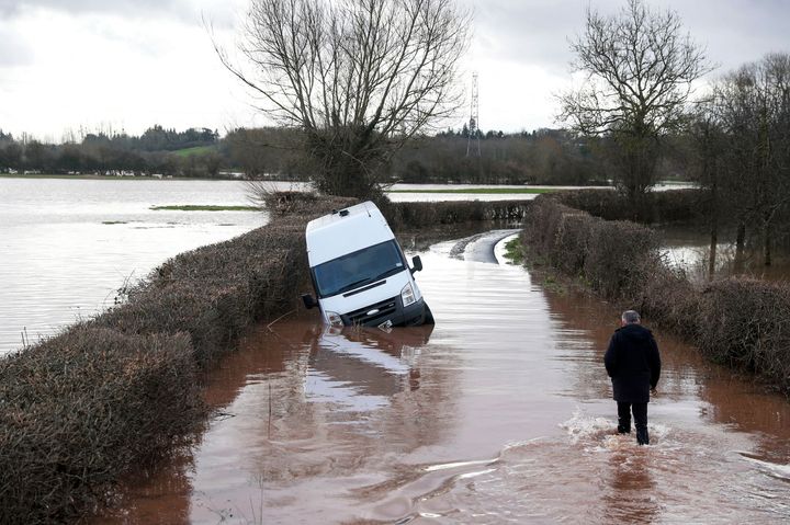 A man makes his through floodwater past an abandoned vehicle near the village of Hampton Bishop near Hereford, after the River Lugg burst its banks.