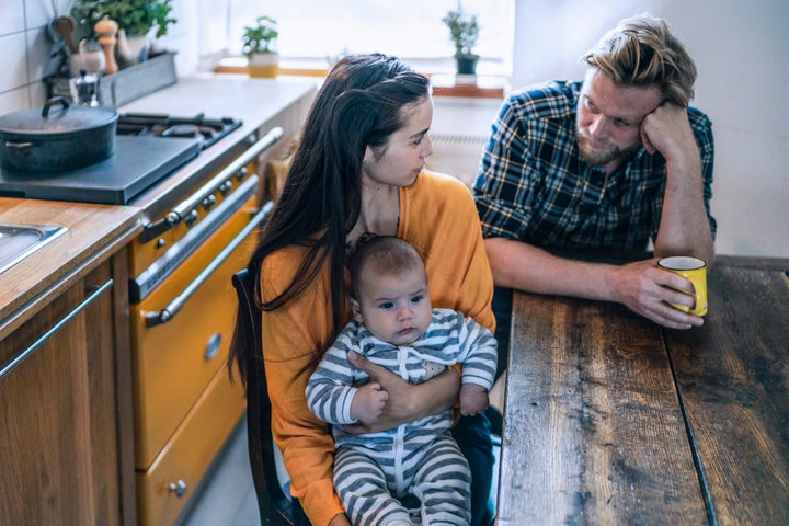 Serious family with baby sitting at kitchen table at home