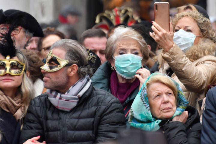 Masks mix with sanitary masks in the last day of carnival, as authorities decided to cut it two days shorter, in Venice, Sunday, Feb. 23, 2020. Italian authorities have announced they are shutting down Venice's famed carnival events in a bid to stop the spread of the novel virus, as numbers of infected persons in the country have soared to at least 133, the largest amount of cases outside Asia. (AP Photo/Luigi Costantini)