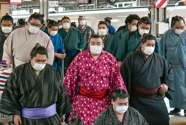 In this Sunday, Feb. 23, 2020, photo, sumo wrestlers wearing masks arrive at Shin Osaka railway station in Osaka, western Japan. A viral outbreak that began in China has infected more than 79,000 people globally. The World Health Organization has named the illness COVID-19, referring to its origin late last year and the coronavirus that causes it.  (Kyodo News via AP)