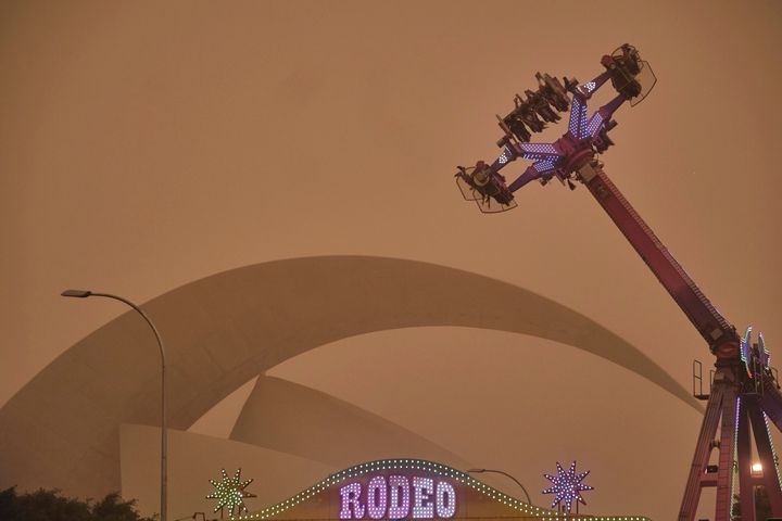 People ride on a fairground attraction in a cloud of red dust in Santa Cruz de Tenerife.