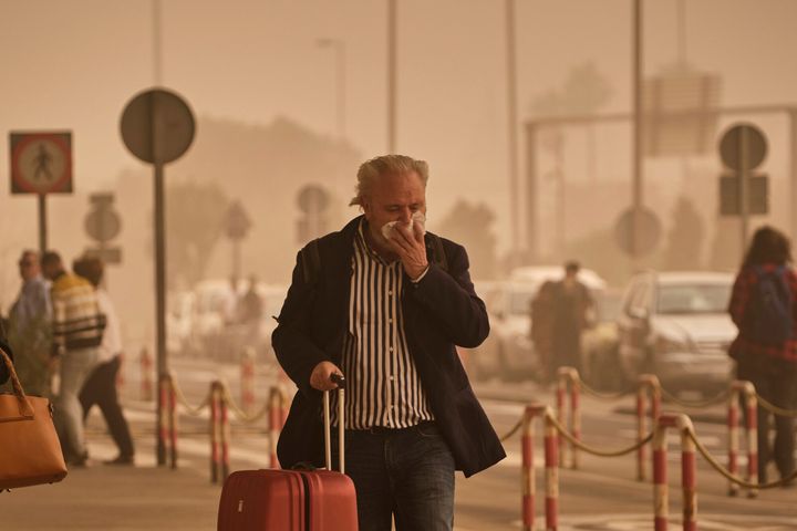 A passenger covers his nose and mouth in a cloud of red dust at the airport in Santa Cruz de Tenerife.