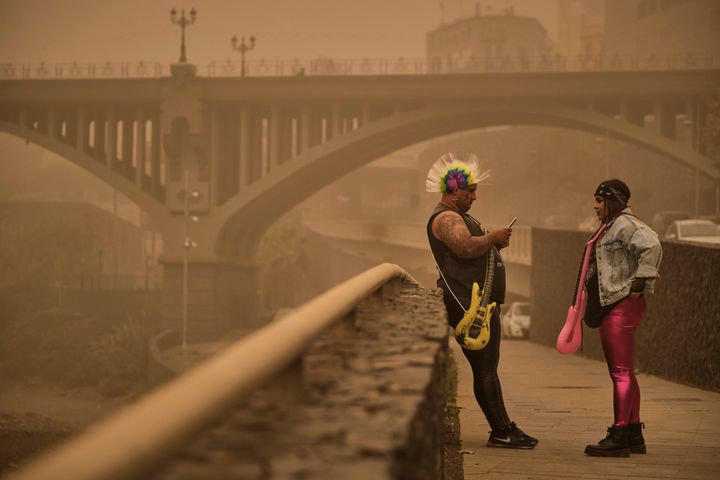 Two people in carnival dress stand beneath a cloud of red dust in Santa Cruz de Tenerife.