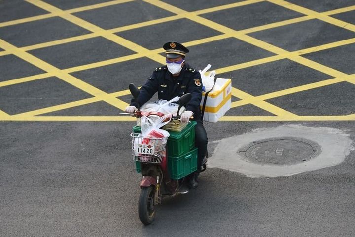 Un hombre con una máscara conduce su motocicleta con alimentos en Wuhan