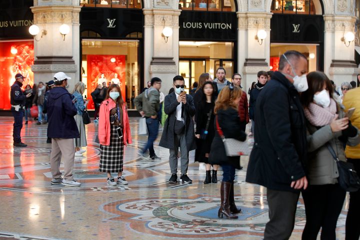 Tourists wearing sanitary masks walk in downtown Milan, Italy, on Sunday. The country has reported Europe's largest number of