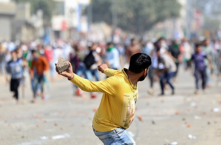 A man supporting the new citizenship law throws a stone at those who are opposing the law, during a clash in New Delhi, February 24, 2020. 