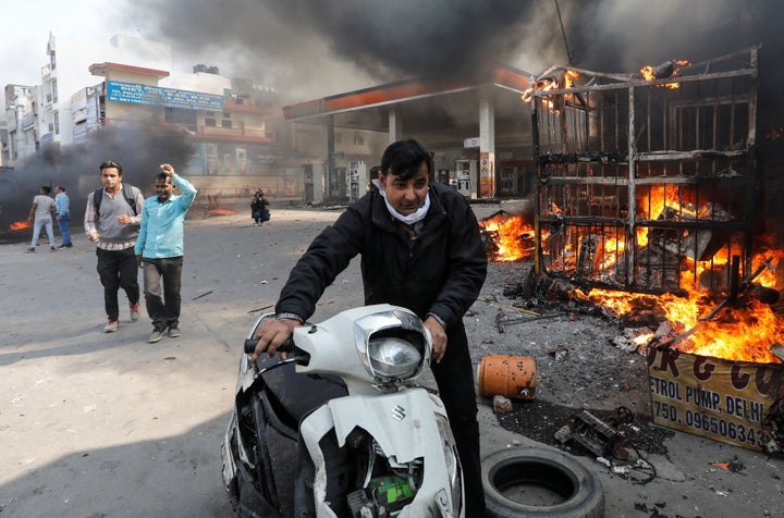 A man pushes his damaged scooter past a burning petrol pump during riots in Delhi.