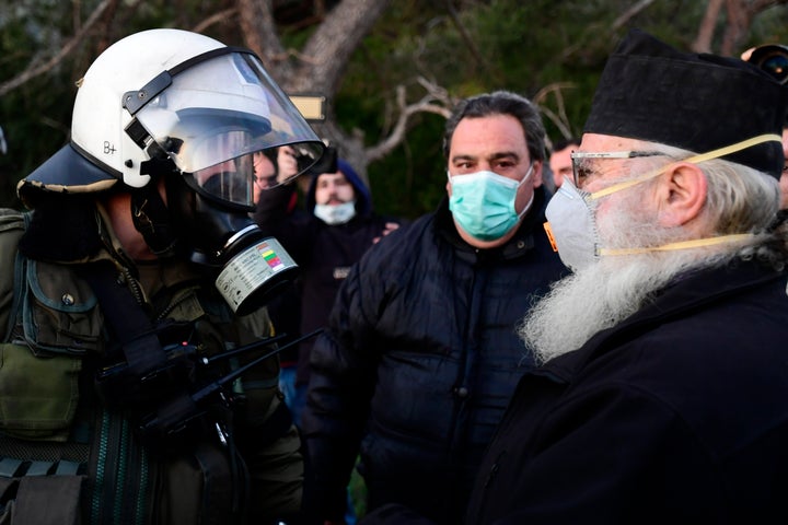 Ενας παπάς με μάσκα που θα μπορούσε να φορά και για τον...κορονοϊό, διαφωνεί πρόσωπο με πρόσωπο με αστυνομικό που φέρει πλήρη εξάρτηση, μέσα στο πολεμικό σκηνικό που στήθηκε γύρω από τη θέση Καραβάς στην Λέσβο, με φόντο τον σχεδιασμό για κατασκευή δομής υποδοχής κλειστού τύπου για μετανάστες και πρόσφυγες. Η τοπική κοινωνία έχει επαναστατήσει κατά αυτού του σχεδίου. (AP Photo/Michael Varaklas)