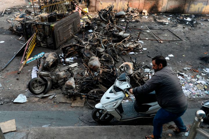 A man makes his way around burnt vehicles after the violence in Delhi. 