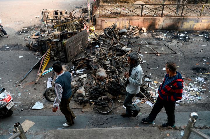 People make their way around burnt vehicles following the violence in Delhi on 25 February.