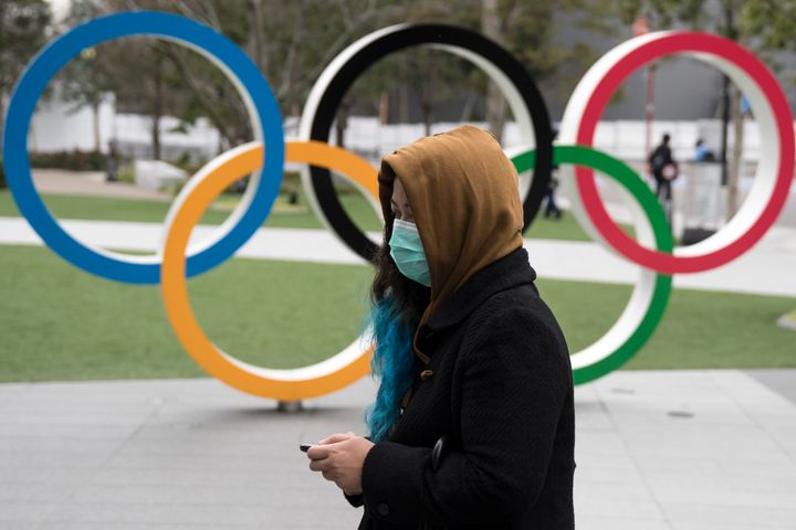 A woman wearing a face mask walks past the Olympic rings in front of the new National Stadium in Tokyo, Japan. 
