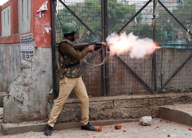 A riot police officer fires tear gas during a protest.