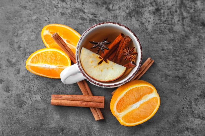 Hot drink with cinnamon sticks and apple in cup on grey background