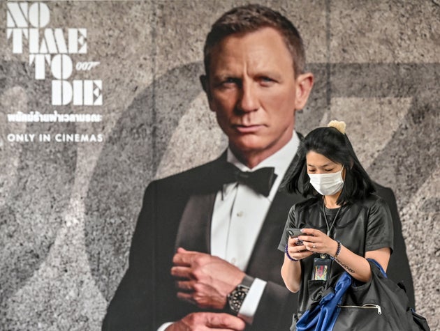 A woman wearing a facemask amid fears of the spread of the COVID-19 novel coronavirus walks past a poster for the new James Bond movie
