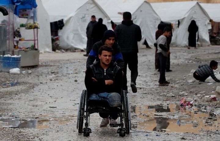 Εκτοπισμένοι πρόσφυγες σπρώχνουν ένα αναπηρικό καρότσι ανάμεσα στις σκηνές καταυλισμού κοντά στο Ιντλίμπ.