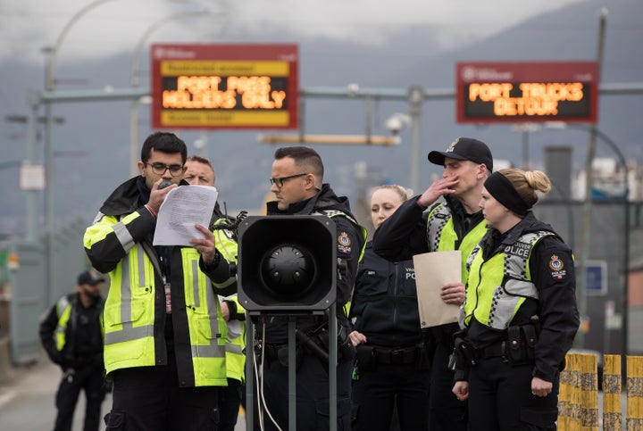 A Port Authority security guard is flanked by police officers as he reads out an injunction against protesters in Vancouver, on Feb. 25, 2020.