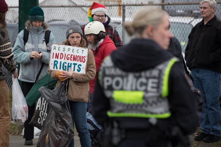 A woman holds a sign as people watch from the sidewalk as police officers prepare to enforce an injunction in Vancouver, on Feb. 25, 2020. 