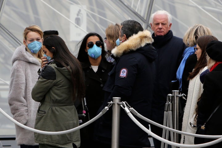 Tourists, some wearing a mask, queue to enter the Louvre museum Friday, Feb. 28, 2020 in Paris. The world is scrambling to get on top of the new coronavirus outbreak that has spread from its epicenter in China to most corners of the planet. Governments and doctors are presenting an array of approaches as the virus disrupts daily routines, business plans and international travel around the world.