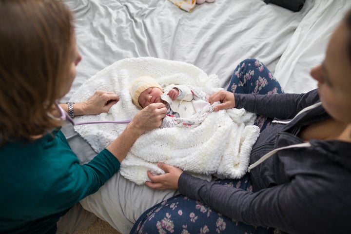 A midwife examines a newborn baby girl alongside her mother in this stock photo.