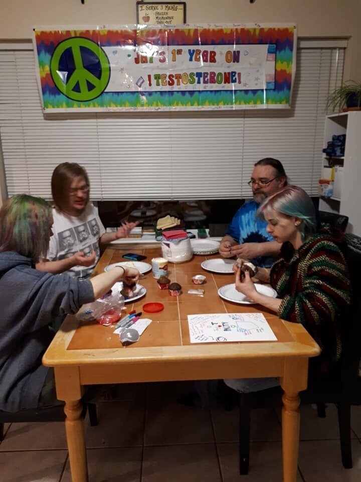 The Scott family and some friends decorate cupcakes for the anniversary party. The banner above the table reads, "Jay's 1st year on testosterone."