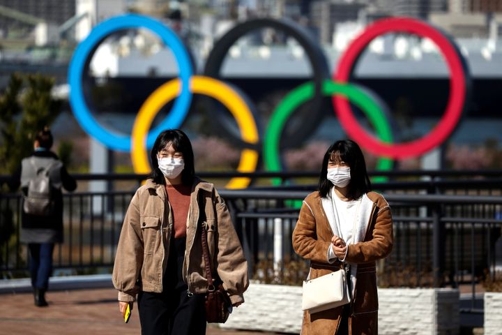 People wearing protective face masks in front of the Giant Olympic rings at the waterfront area at Odaiba Marine Park in Tokyo, Japan