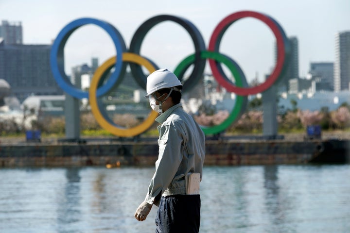 A masked man works at a construction site with the Olympic rings in the background on Tuesday, March 3, 2020, at Tokyo's Odaiba district in Tokyo.