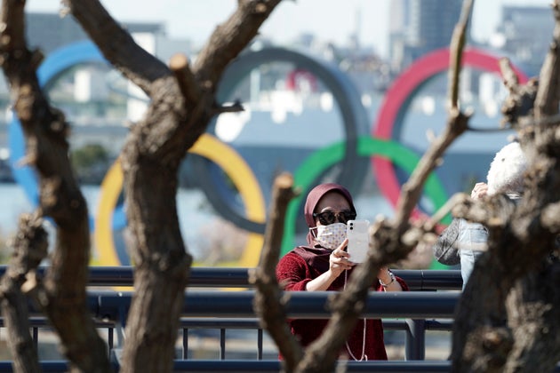 A tourist wearing a protective mask takes a photo with the Olympic rings in the background in Tokyo on...