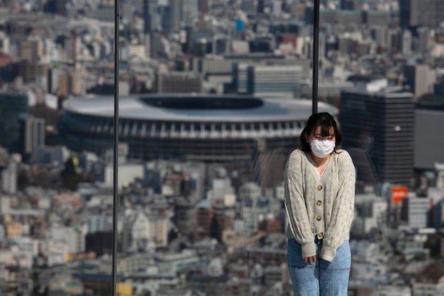 A woman with a mask pauses for photos on Shibuya Sky observation deck as the New National Stadium, a...