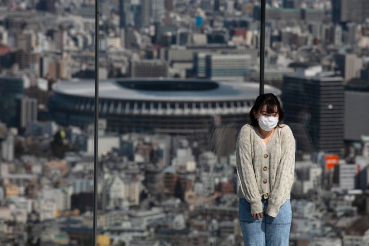 A woman with a mask pauses for photos on Shibuya Sky observation deck as the New National Stadium, a venue for the opening an